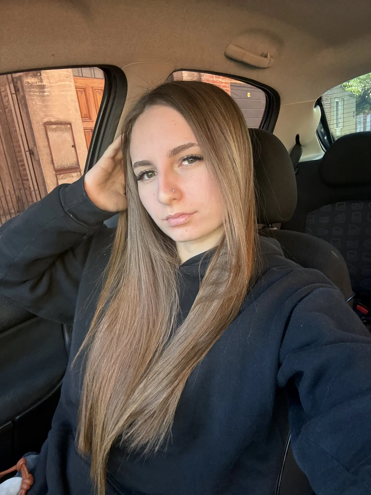 Teya sitting in her car, wearing a black hoodie